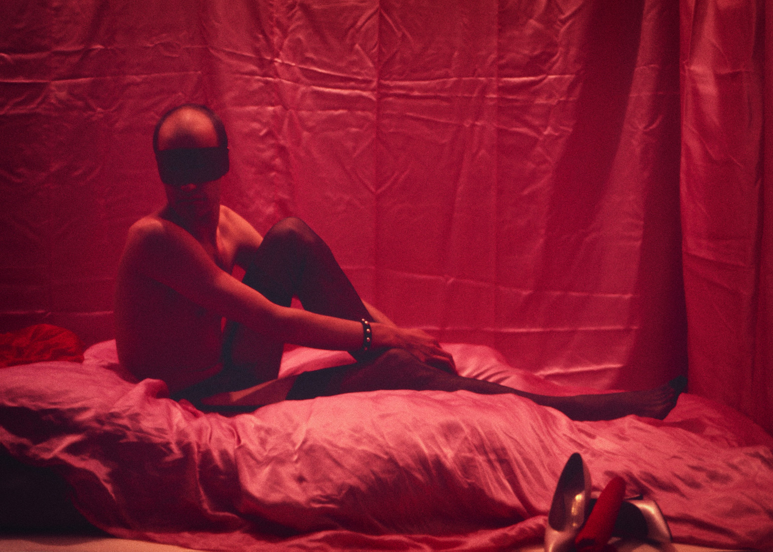 Masked artist posing on pink satin sheets